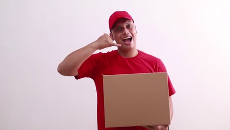 Young-asian-courier-man-holding-cardboard-while-making-phone-hand-gesture