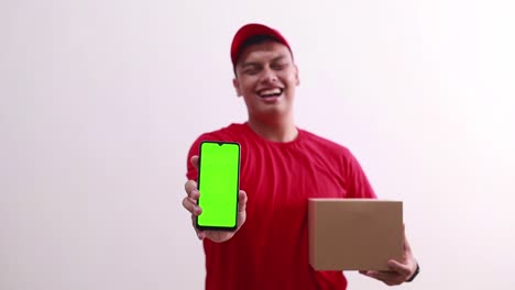 Young-asian-deliveryman-holding-cardboard-while-showing-green-screen-phone-display