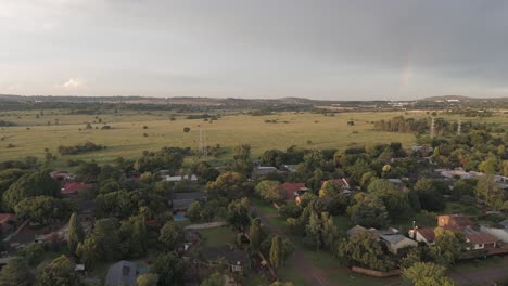 Aerial-4k,-flying-over-a-cityscape-of-residential-homes,-moving-towards-an-open-field-with-a-hint-of-a-rainbow-in-the-sky,-Centurion,-South-Africa