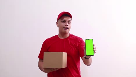 Young-asian-courier-man-standing-holding-cardboard-while-showing-green-screen-blank-phone-display