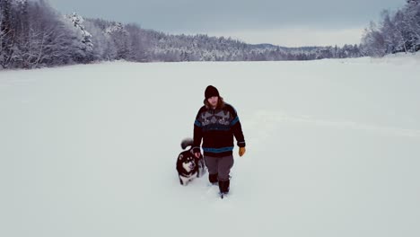 Un-Hombre-Vestido-De-Invierno-Camina-En-La-Nieve-Profunda-Con-Su-Perro-Malamute-De-Alaska