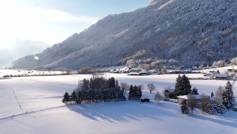 River-covered-with-snow-near-the-village-during-winter-season-near-the-mountain,-aerial-ascending