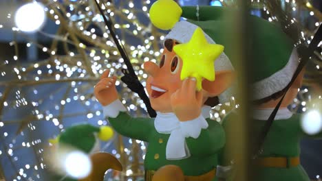 Close-up-of-happy-smiling-christmas-elf-models-sat-smiling-inside-a-cage-of-christmas-glowing-warm-fairy-lights-as-foreground-and-background