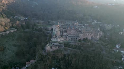 Aerial-view-of-a-historic-castle,-nestled-in-a-forest-of-lush-trees,-as-a-sunbeam-shines