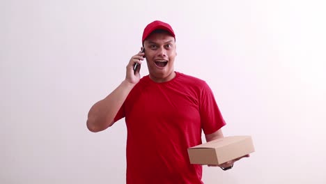Young-asian-courier-man-holding-a-cardboard-while-talking-on-the-phone