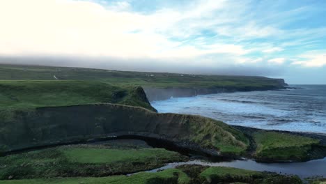 Wild-green-Irish-coast-with-rough-sea-waves-crashing-on-cliffs-in-background,-Doolin-in-Ireland