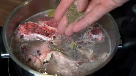 Person-adding-thyme-to-pot-of-bone-broth-cooking-on-stove-in-home-kitchen