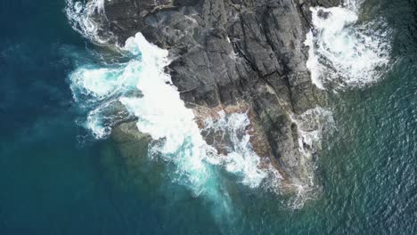 Scenic-aerial-top-down-view-of-turquoise-ocean-waves-crashing-against-coastal-rocks