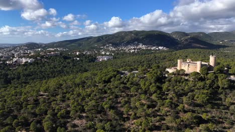 Toma-Aérea-Acercándose-Al-Paisaje-Verde-De-Las-Montañas-Y-Al-Histórico-Castillo-Castell-De-Belver-En-Mallorca