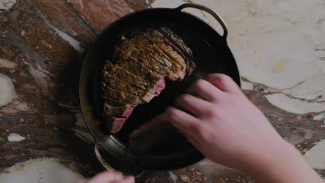 Top-down-shot-of-a-ribeye-steak-being-plated-into-a-cast-iron-pan