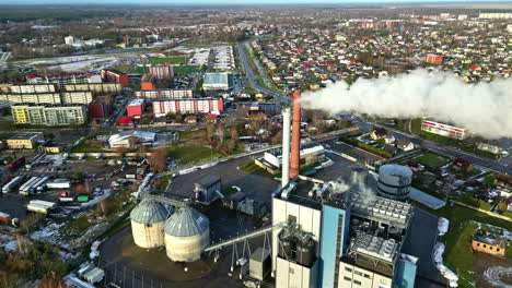 Local-factory-emitting-smoke-near-small-township,-aerial-orbit-view