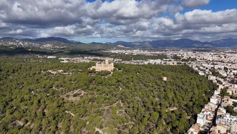 Aerial-wide-shot-showing-Castel-de-Bellver-on-hill-and-cityscape-of-Palma-in-Background,-Mallorca
