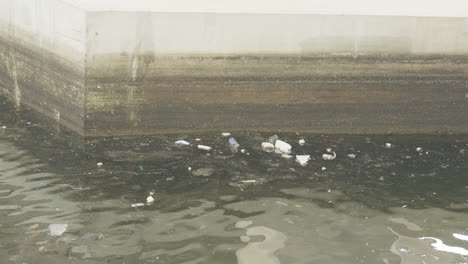 Debris-and-floatsam-of-styrofoam-cups-and-plastic-float-against-concrete-canal-wall