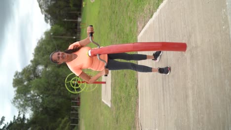 The-Woman-is-Utilizing-a-Hand-Pedal-Exerciser-While-in-the-Park---Vertical-Shot