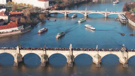Aerial-view-of-Charles-bridge-over-river-and-multiple-tourist-boats-float