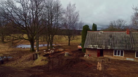 Industrial-digger-working-in-remote-countryside-homestead,-aerial-follow-view