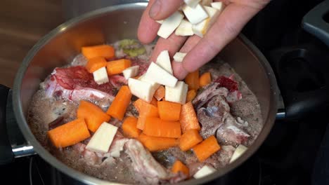Person-adding-chopped-parsnips-to-bone-broth-beginning-to-boil-in-pot