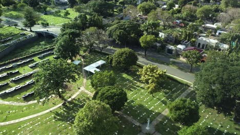 Drohnenaufnahme-Des-Philippinischen-Gedenkfriedhofs,-Voller-Bäume,-Mit-Vorbeifahrenden-Autos