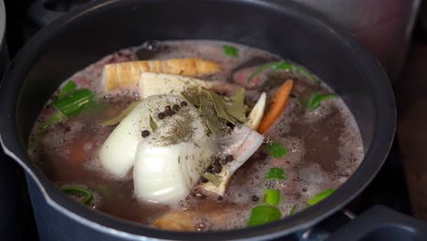 Pot-of-bone-broth,-with-vegetables-and-seasoning,-simmering-slowly-in-large-pot