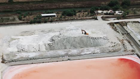 Aerial-view-of-excavator-on-pile-of-salt,-sea-salt-farm-infrastructure,-Albania