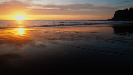 Ein-Atemberaubender-Sonnenuntergang-Zeichnet-Den-Himmel-über-Einen-Ruhigen-Strand-Mit-Majestätischen-Klippen