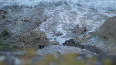 Closeup-shot-of-continuous-small-tides-hitting-stones-at-the-shoreline-during-daytime