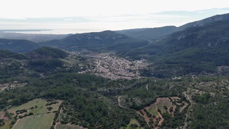 Aerial-backwards-flight-over-green-hills-of-Mallorca-and-Esporles-Village-in-the-valley-during-daytime