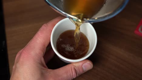 Person-pouring-hot-bone-broth-from-pan-into-mug,-slow-motion-top-down-view