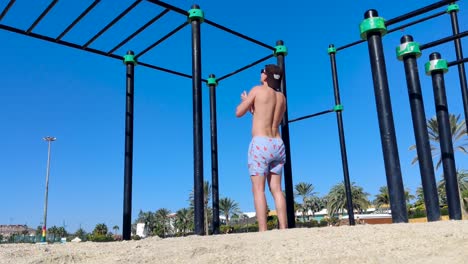 Mann-Macht-Klimmzüge,-Outdoor-Trainingsort-An-Einem-Sonnigen-Strand,-Fitter-Kaukasischer-Mann-Beim-Calisthenics-Training-Mit-Dem-Eigenen-Körpergewicht,-Aufgenommen-Auf-Fuerteventura