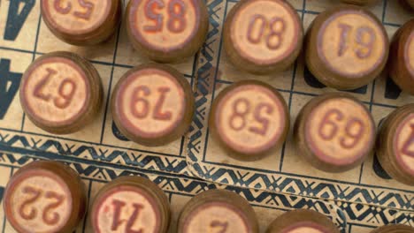 Cinematic-close-up-smooth-shot-from-above-of-a-pile-of-Bingo-wooden-barrels-in-a-row,-woody-figures,-old-numbers-background,-vintage-board-game,-4K-commercial-rotating-zoom-out-gimbal-video