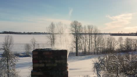 Close-up-of-cottage-brick-chimney-with-smoke-come-out,-snowy-winter-landscape