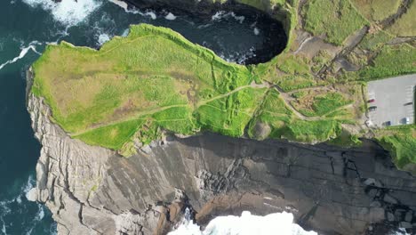 Aerial-drone-shot-flying-over-the-coastal-Kilkee-Cliffs,-in-County-Clare-Ireland,-with-views-of-waves-crushing-over-the-rugged-coastline