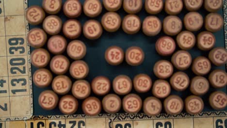 Cinematic-close-up-smooth-shot-from-above-of-a-pile-of-Bingo-wooden-barrels-in-a-square,-woody-figures,-old-numbers-background,-vintage-board-game,-slow-motion-120-FPS-commercial-zoom-out-gimbal-video