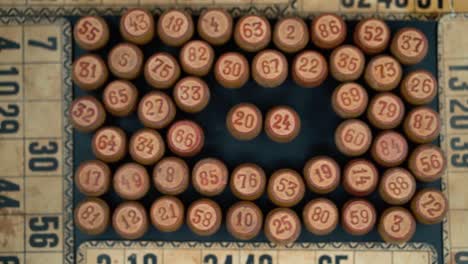 Cinematic-close-up-smooth-shot-from-above-of-a-pile-of-Bingo-wooden-barrels-in-a-square,-woody-figures,-old-numbers-background,-vintage-board-game,-slow-motion-120-FPS-commercial-video-pan-left
