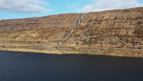 Vista-Aérea-Del-Agua-Cayendo-Sobre-Una-Cascada-En-Una-Pared-De-Montaña-Seca-En-Islandia