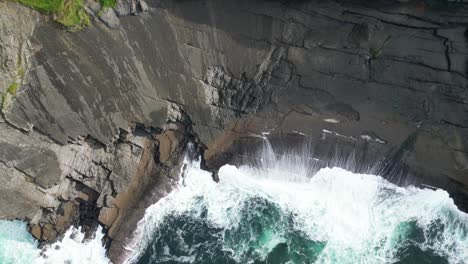 Aerial-drone-shot-revealing-coastal-Kilkee-Cliffs-in-Ireland-where-waves-are-crushing-against-the-high-rocky-cliffs