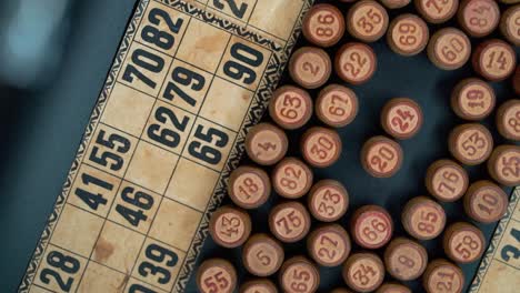 Cinematic-close-up-smooth-shot-from-above-of-a-pile-of-Bingo-wooden-barrels-in-a-square,-woody-figures,-old-numbers-background,-vintage-board-game,-slow-motion-120-FPS-commercial-rotating-gimbal-video