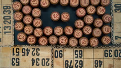 Cinematic-close-up-smooth-shot-from-above-of-a-pile-of-Bingo-wooden-barrels-in-a-square,-woody-figures,-old-numbers-background,-vintage-board-game,-slow-motion-120-FPS-zoom-out-gimbal-video