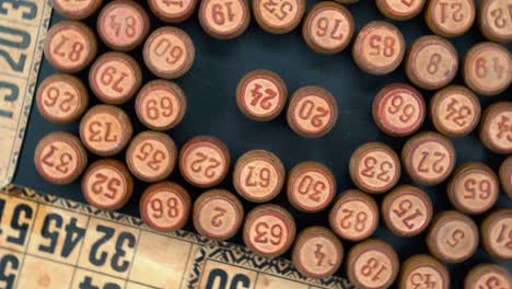 Cinematic-close-up-rotating-smooth-shot-from-above-of-a-pile-of-Bingo-wooden-barrels-in-a-square,-woody-figures,-old-numbers-background,-vintage-board-game,-professional-lighting,-4K-video