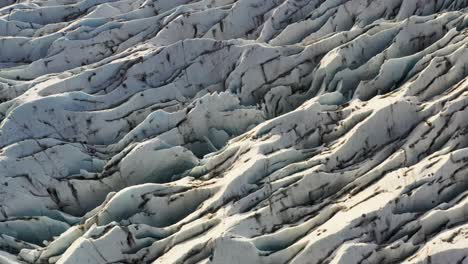 Zoomed-lifting-shot-of-wavy-ice-on-a-frozen-glacier-illuminated-by-sunlight