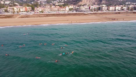 Swimmers-in-the-sea-near-Castelldefels-beach-in-Barcelona,-coastal-cityscape-in-the-background,-daytime,-aerial-view