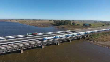 Aerial-view-of-a-passenger-train-crossing-a-bridge-over-a-river,-outskirts-of-Buenos-Aires