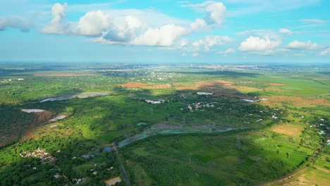 Lush-green-landscape-with-scattered-buildings-and-a-cloudy-sky,-daytime,-aerial-view
