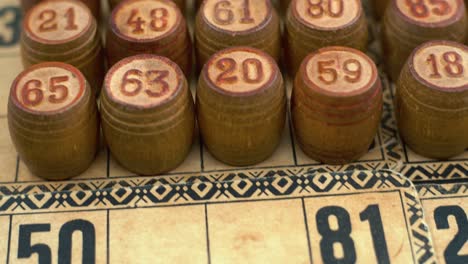 Cinematic-close-up-smooth-forward-shot-from-above-of-Bingo-wooden-barrels-in-a-row,-woody-figures,-old-numbers-background,-vintage-board-game,-4K-commercial-rotating-gimbal-video