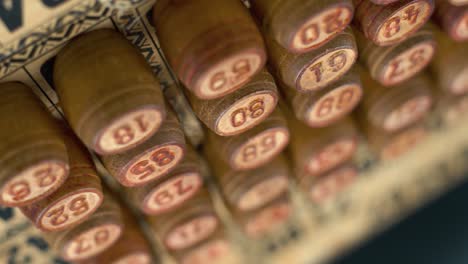 Cinematic-close-up-smooth-dreamy-backwards-shot-from-above-of-Bingo-wooden-barrels-in-a-row,-woody-figures,-old-numbers-background,-vintage-board-game,-4K-commercial-rotating-gimbal-video