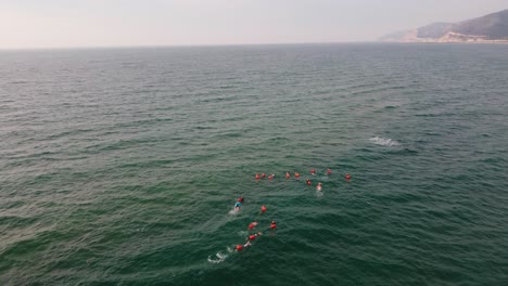 Gruppe-Von-Schwimmern-In-Einer-Formation-Am-Strand-Von-Castelldefels,-Barcelona,-Ruhige-See,-Luftaufnahme