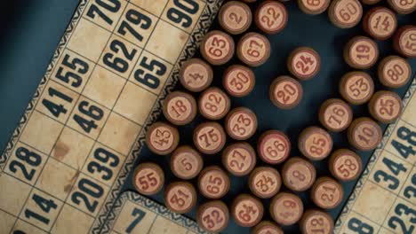 Cinematic-close-up-smooth-shot-from-above-of-a-pile-of-Bingo-wooden-barrels-in-a-square,-woody-figures,-old-numbers-background,-vintage-board-game,-slow-motion-120-FPS-commercial-rotating-gimbal-video