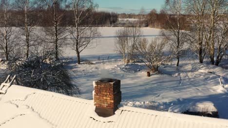 Aerial-view-of-snowy-cottage-roof-with-smoke-come-from-chimney,-winter