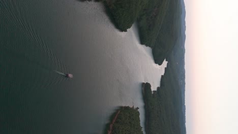 Vertical-aerial-view-of-small-boat-on-Albanian-river-near-forest-hillside