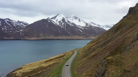 Aeriall-lifting-view-of-a-car-driving-over-a-road-in-a-fjord-of-Iceland-in-autumn